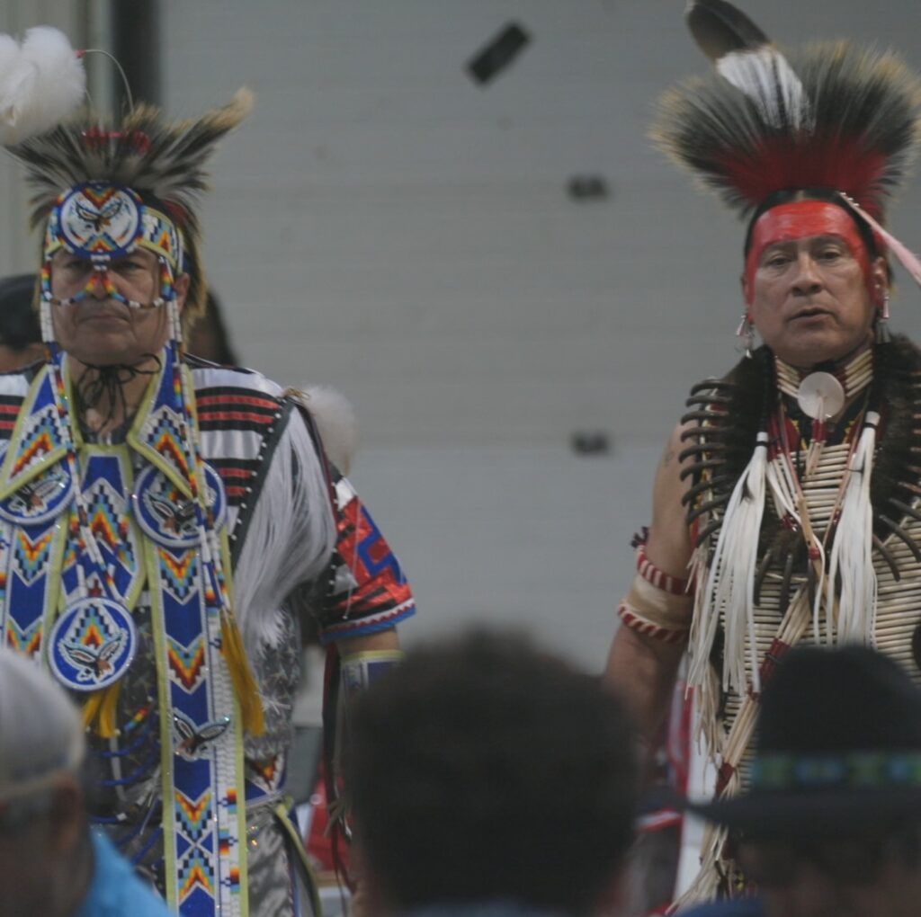 Two Indigenous men wearing traditional feather regalia during a round dance, reflecting Indigenous presence and history along Route 66