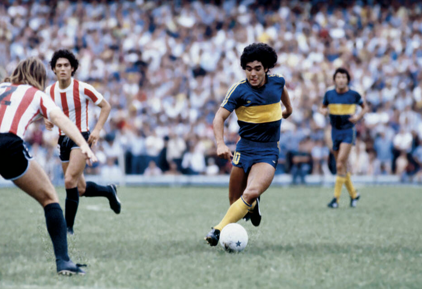 Young Diego Maradona dribbling with the ball close to his left foot while playing for Boca Juniors.
